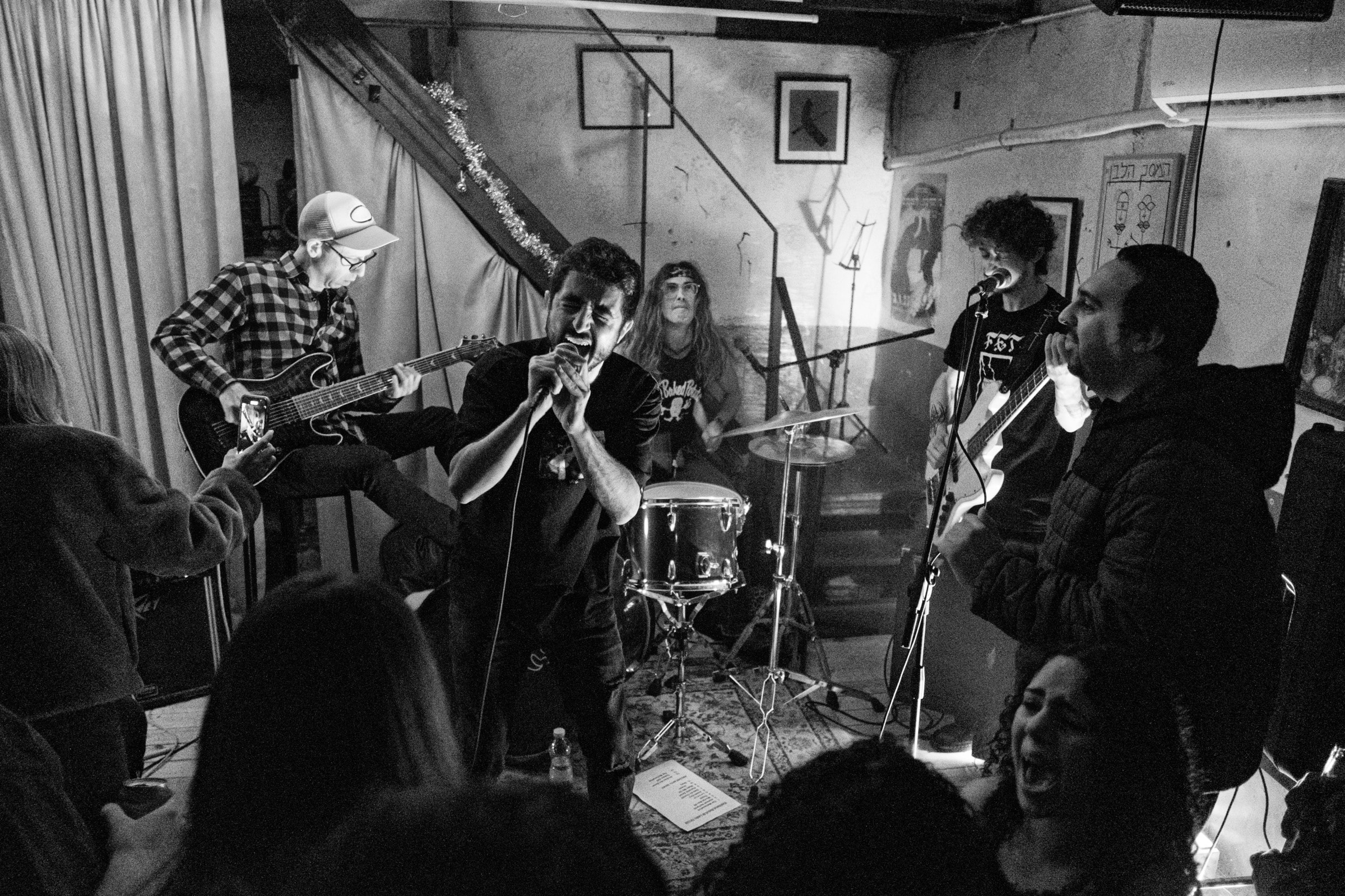 A band plays in a packed basement, guitarist in plaid, singer gripping the mic, crowd laughing in the front row