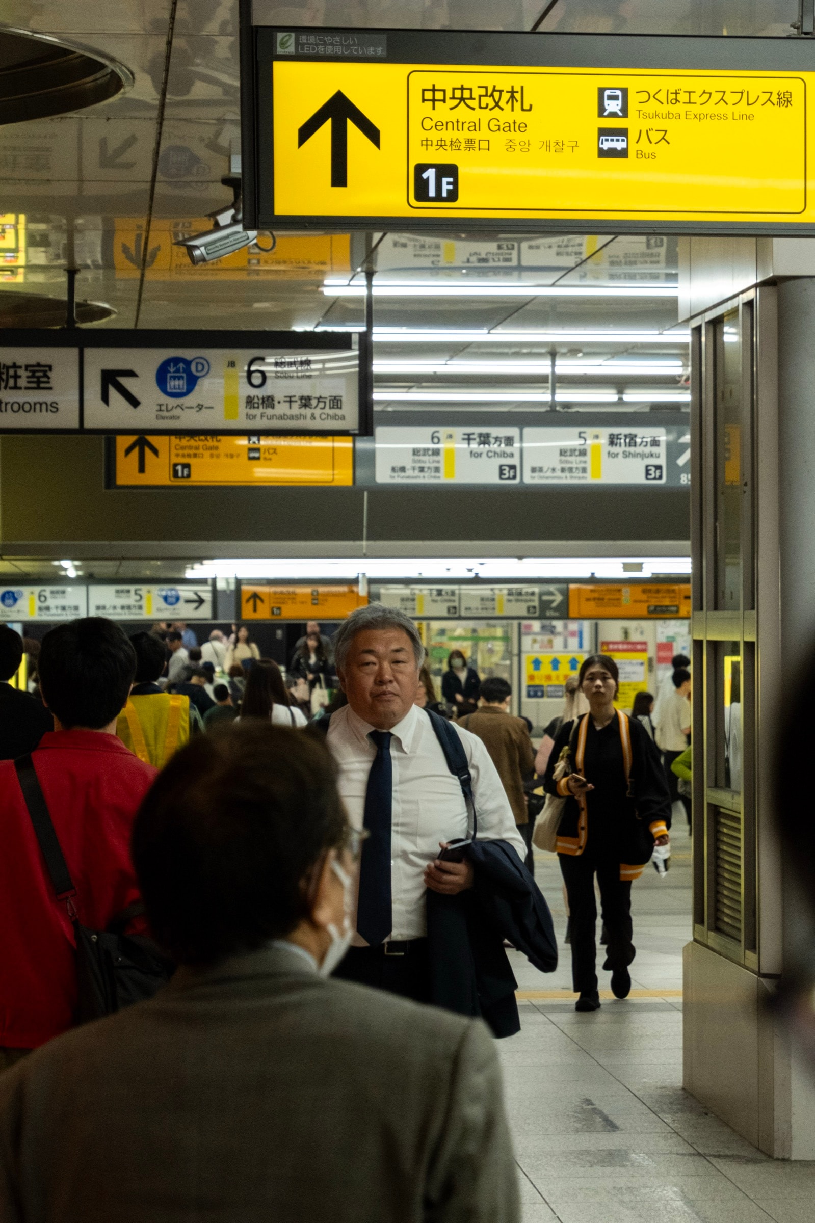 A businessman carrying his jacket walks through a crowded station concourse under yellow Central Gate signs