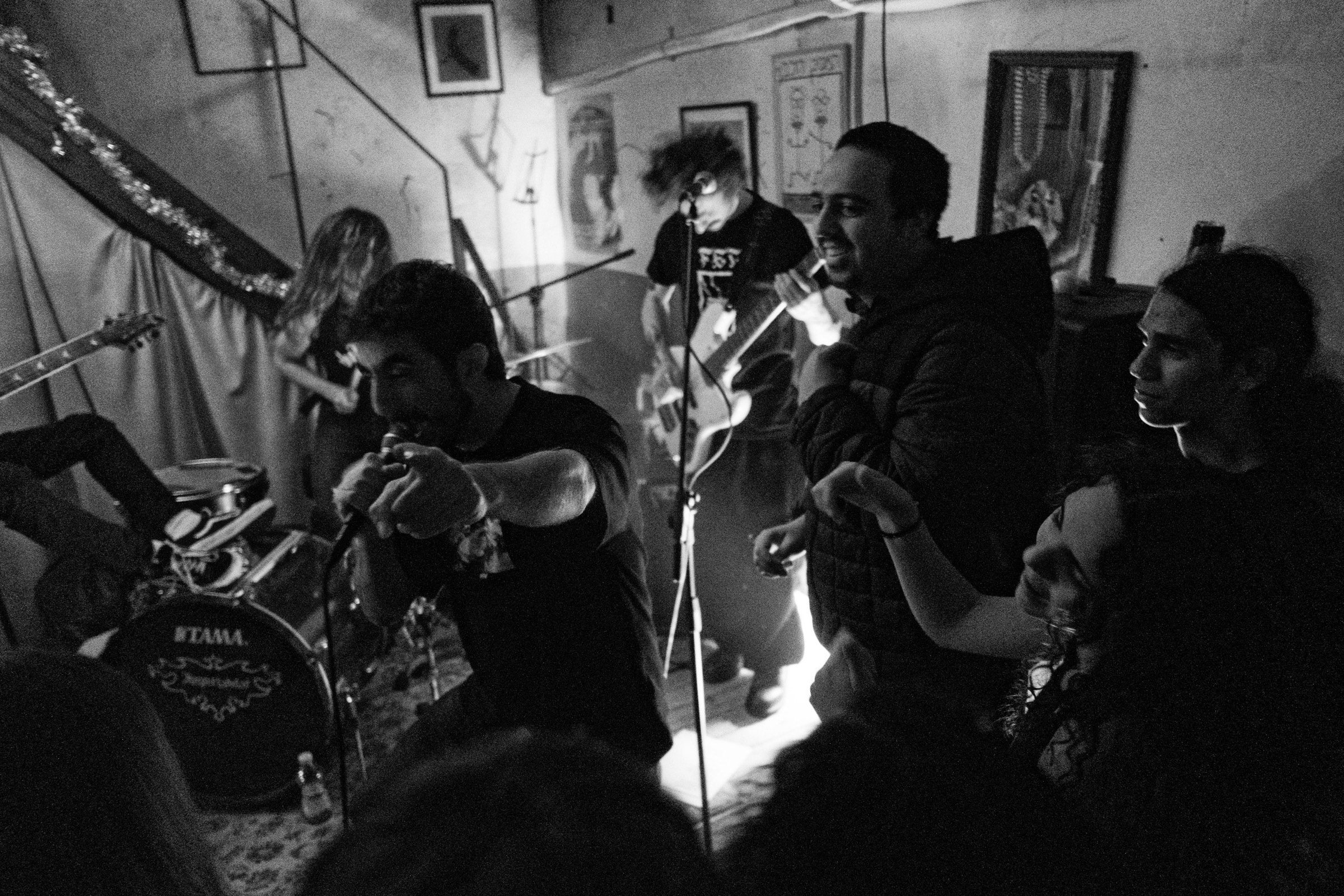 Musicians thrash on a small basement stage, singer leaning into the crowd with a Tama drum kit behind