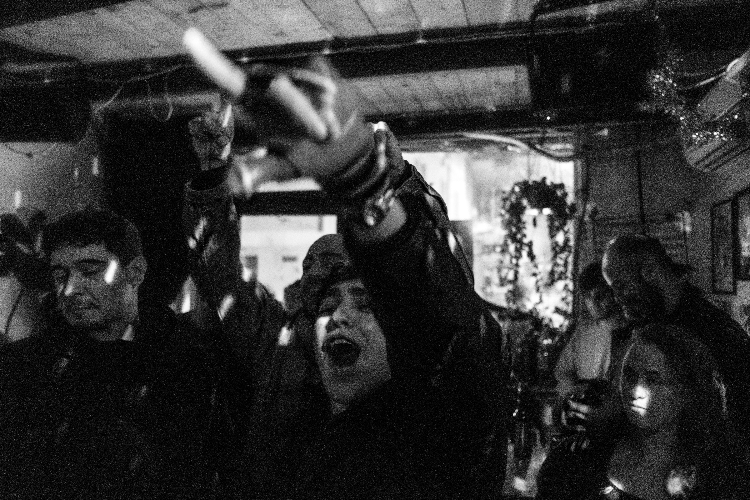 A woman throws her arms up and shouts in a crowd of ecstatic concertgoers in a dim bar