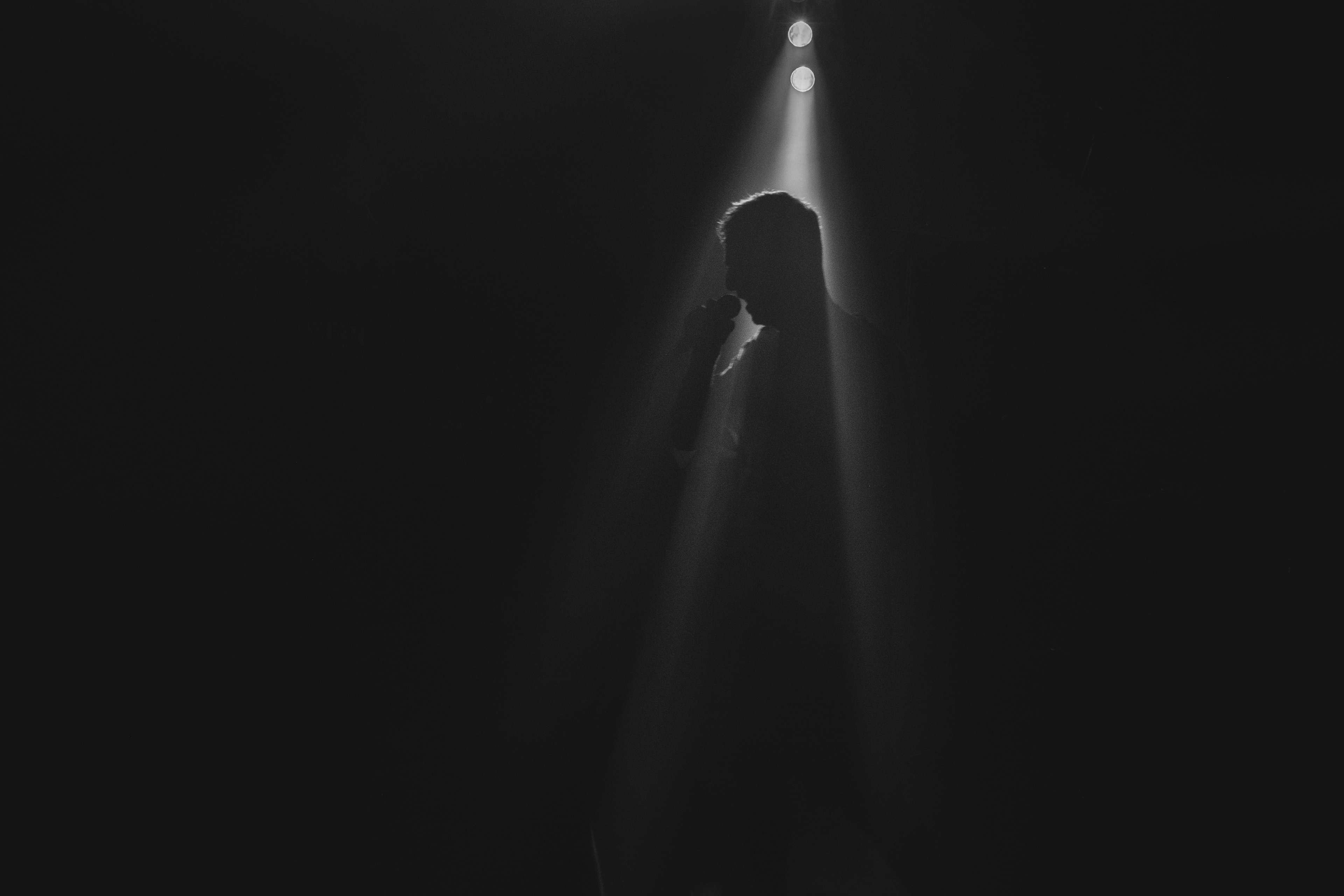 A silhouetted singer stands alone in a beam of spotlight, surrounded by darkness