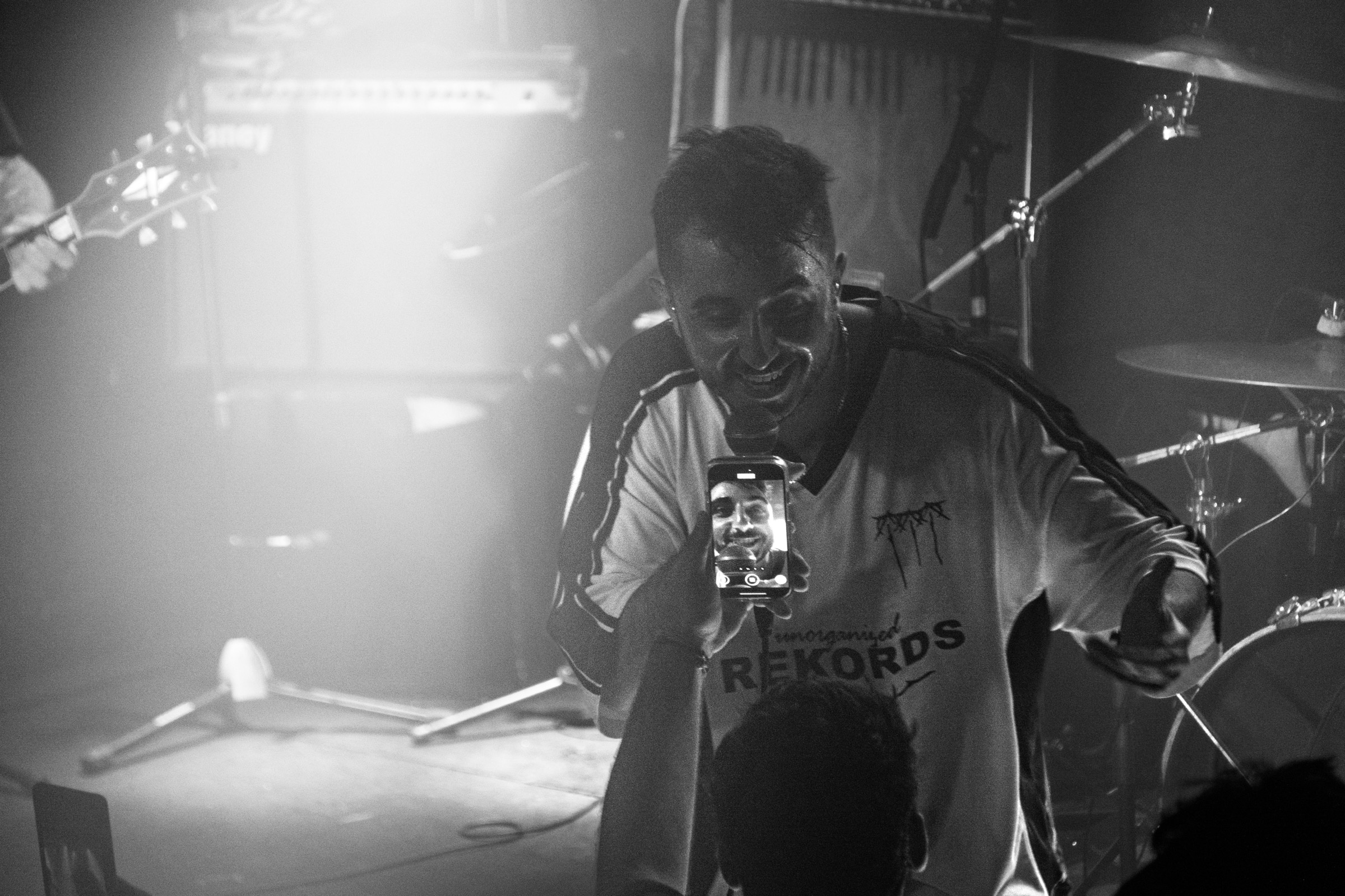 A smiling performer in a Rekords t-shirt leans toward the crowd under hazy stage lighting