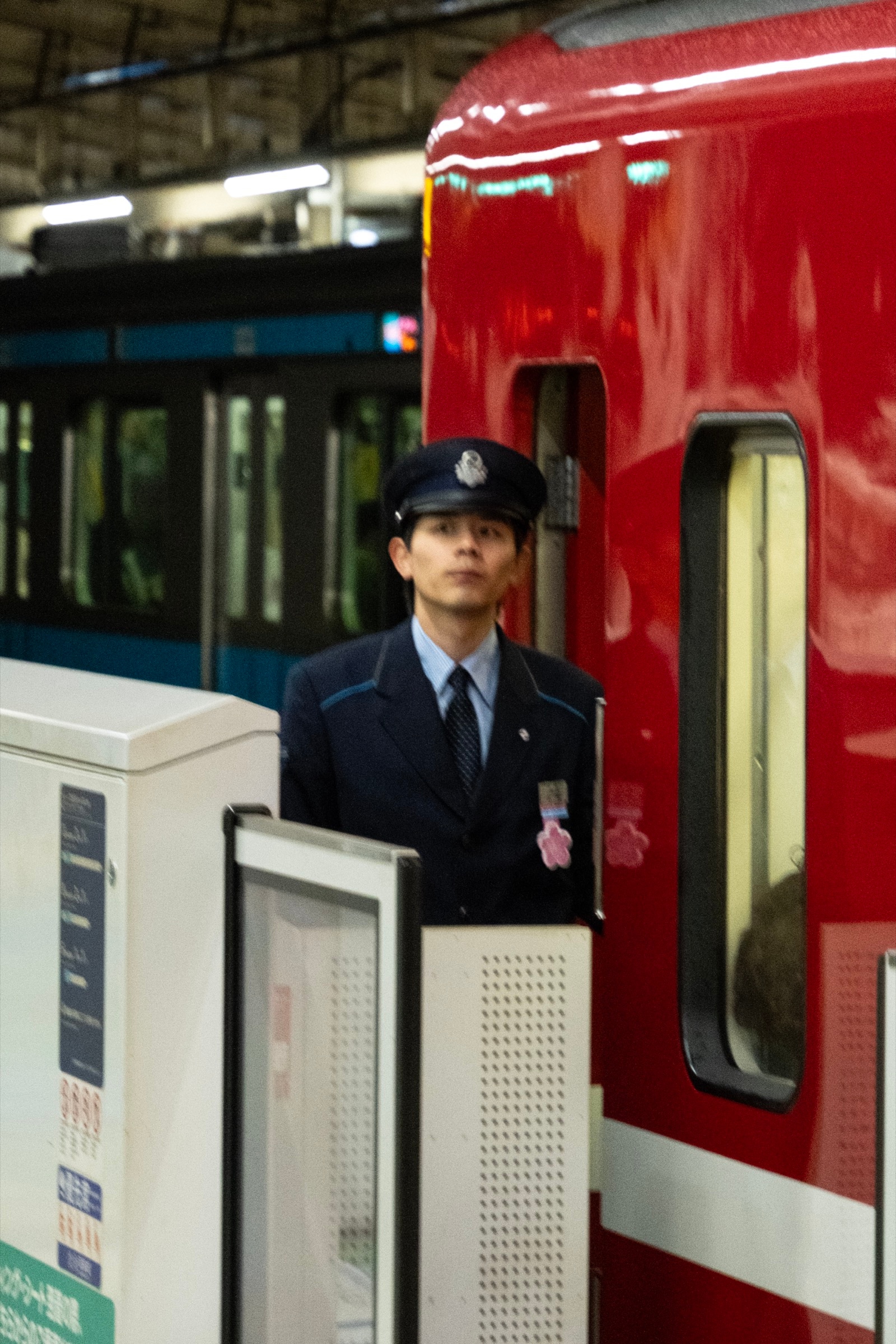 A young train conductor in a navy uniform and cap stands at attention beside a red train car on a platform